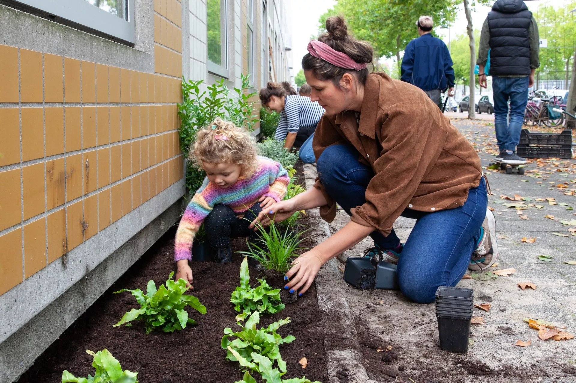 Volwassen vrouw en kind planten samen bloemen in een geveltuin.
