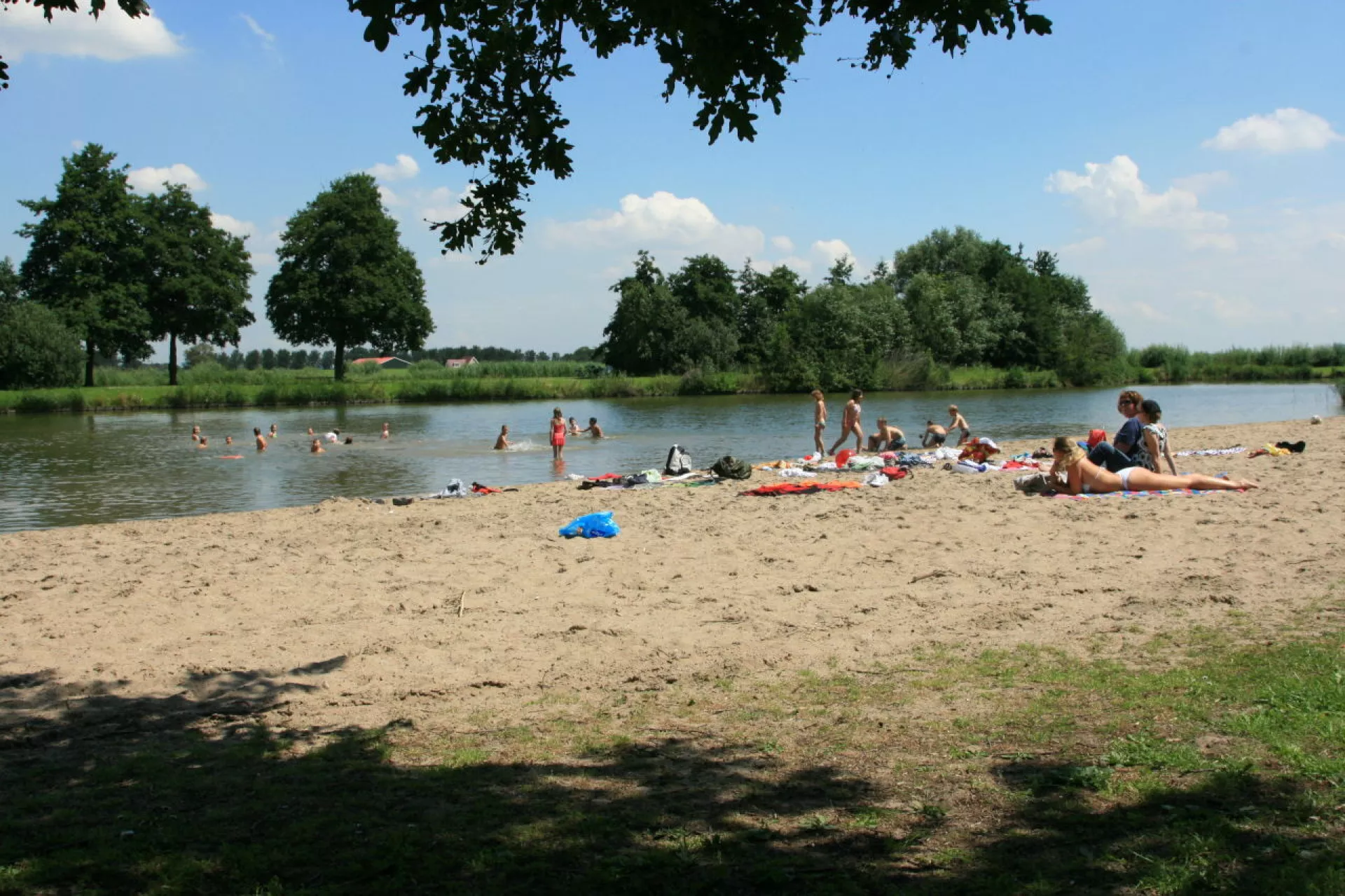 Strand met mensen die genieten van de zon en zwemmen in een meer.