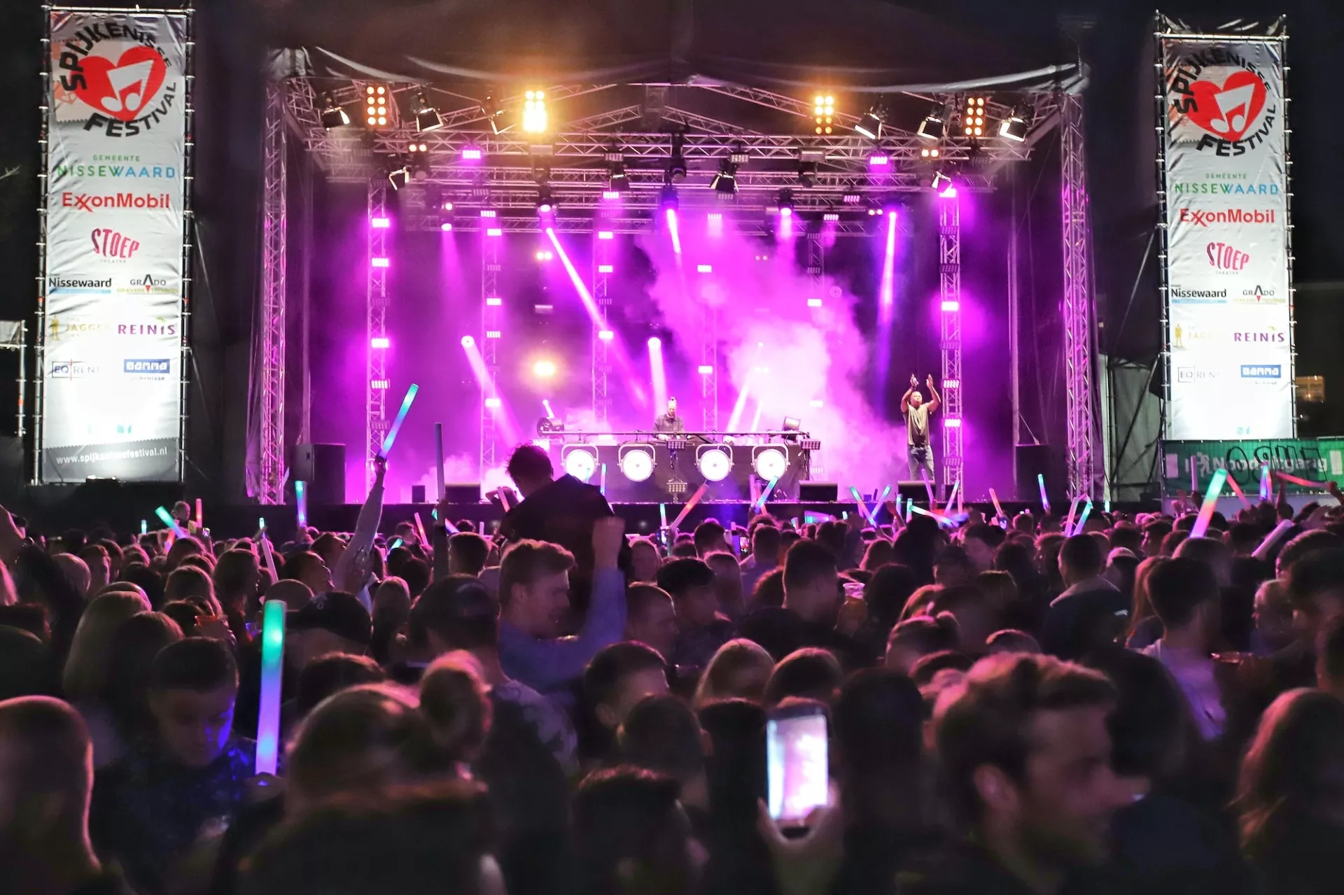 Een menigte geniet van een concert met kleurrijke lichten op het podium.