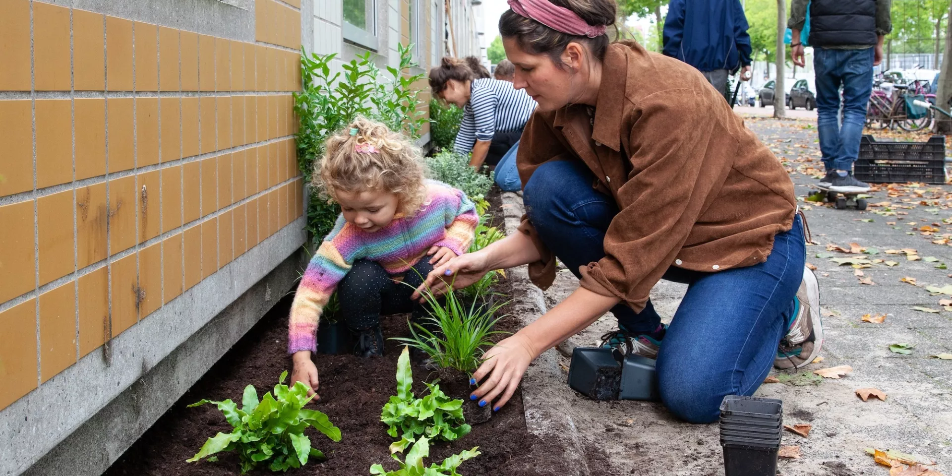 Volwassen vrouw en kind planten samen bloemen in een geveltuin.