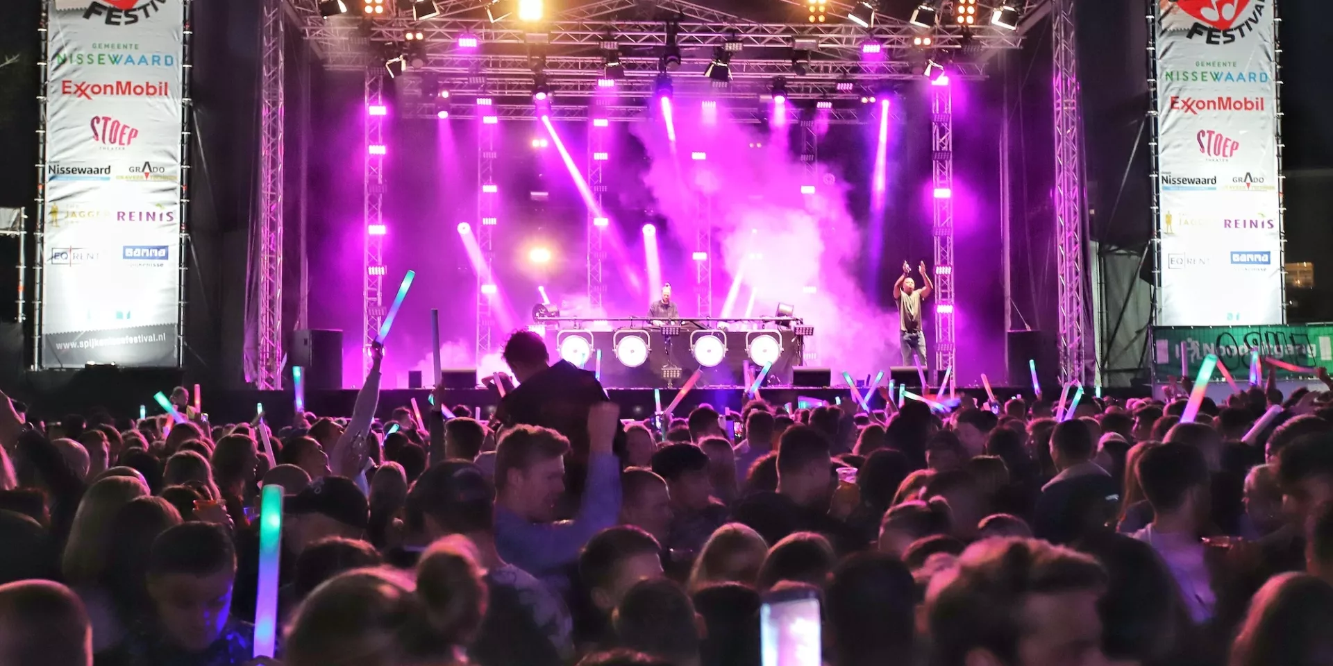 Een menigte geniet van een concert met kleurrijke lichten op het podium.