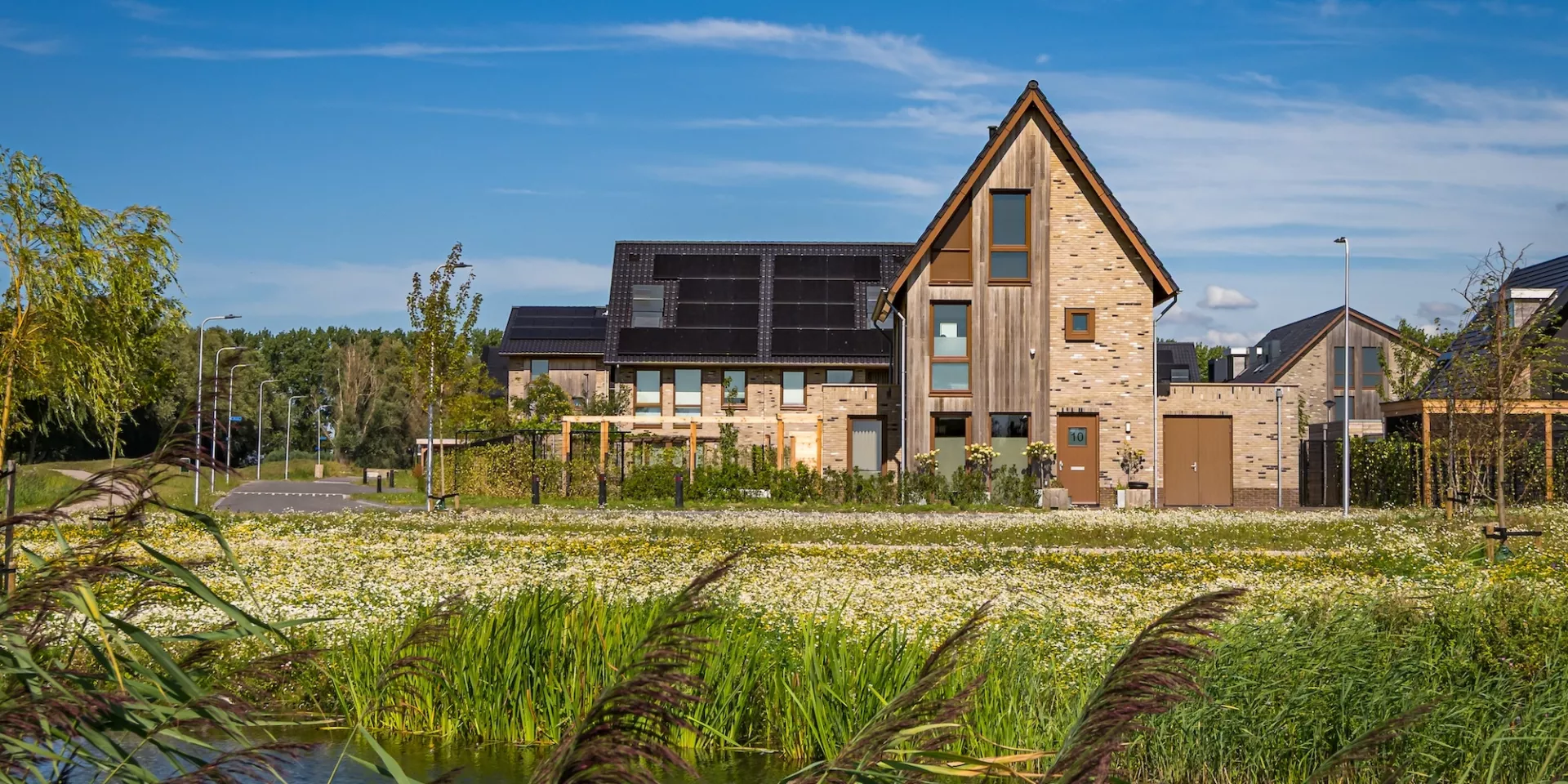 Een modern huis aan het water met een groene omgeving.