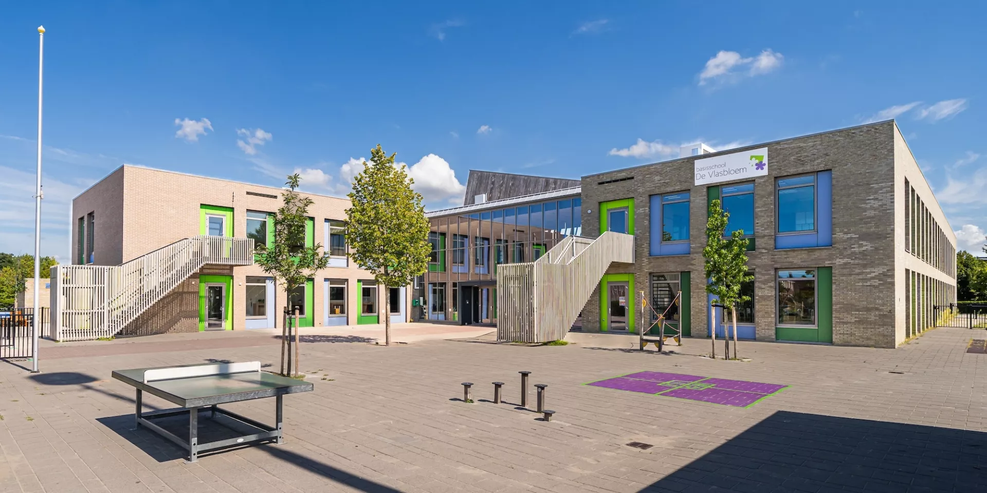 Modern schoolgebouw met speelplaats en kleurrijke ramen.